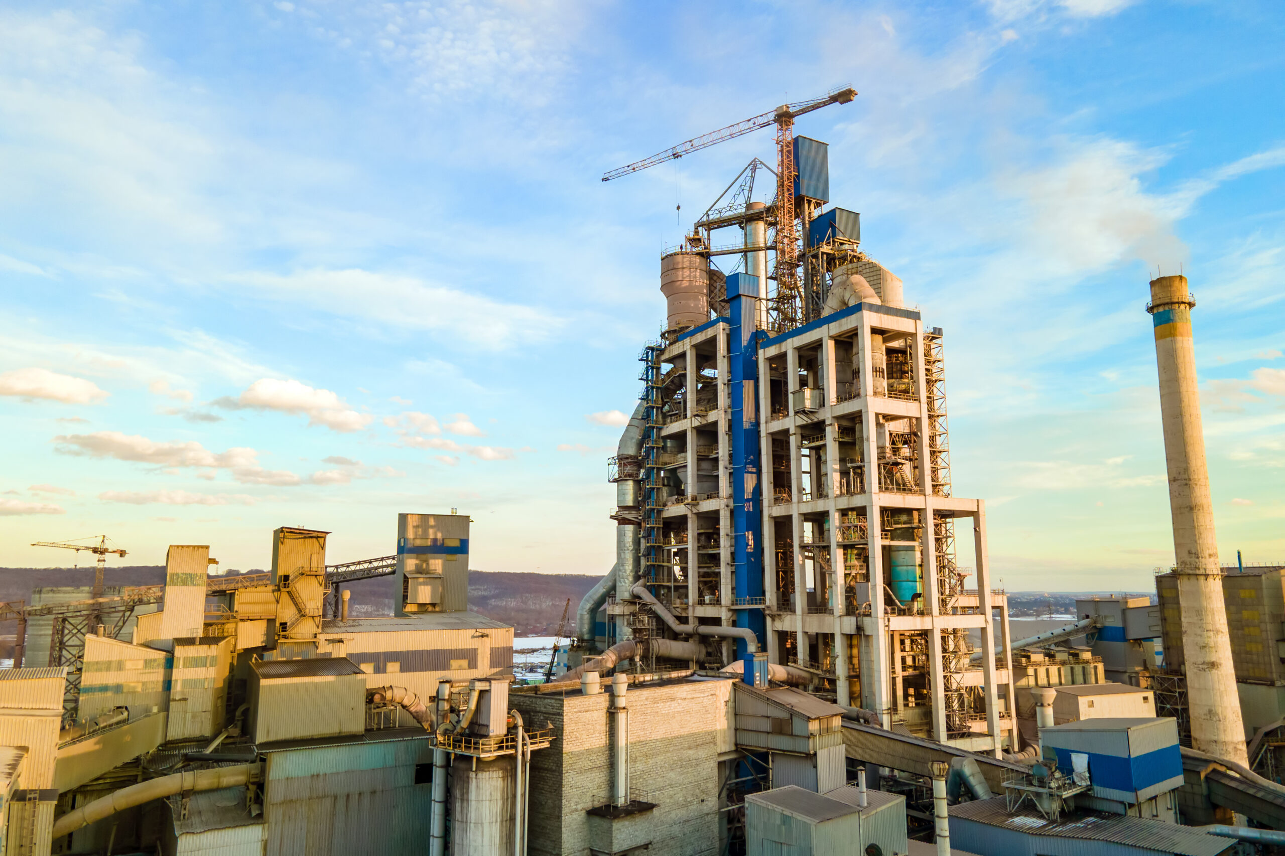 Aerial view of cement plant with high factory structure and tower crane at industrial production area at sunset.